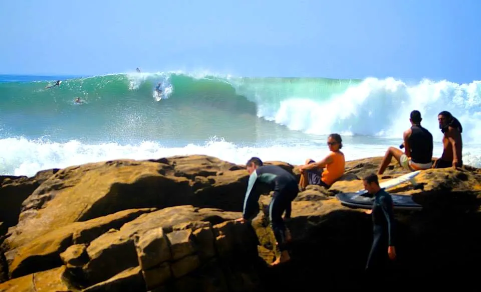 Surfers watching a large wave from the rocks at Anchor Point